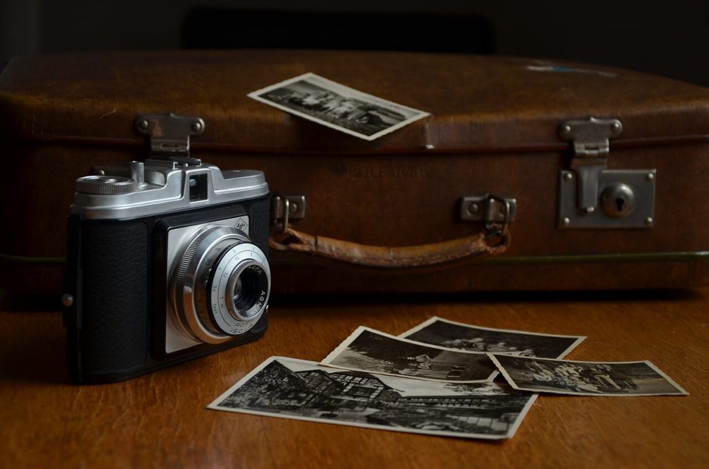 Imagen de una cámara antigua colocada sobre una mesa, acompañada de algunas fotografías en blanco y negro.