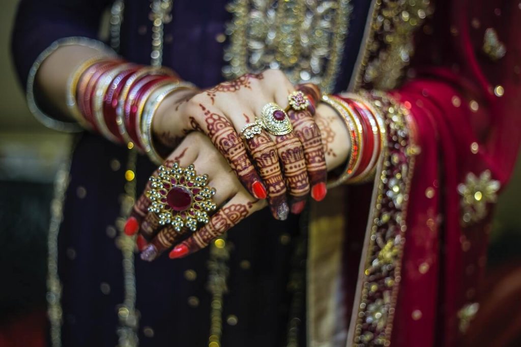 Imagen de una mujer india vestida con vibrantes trajes tradicionales y luciendo intrincados diseños de henna en las manos.